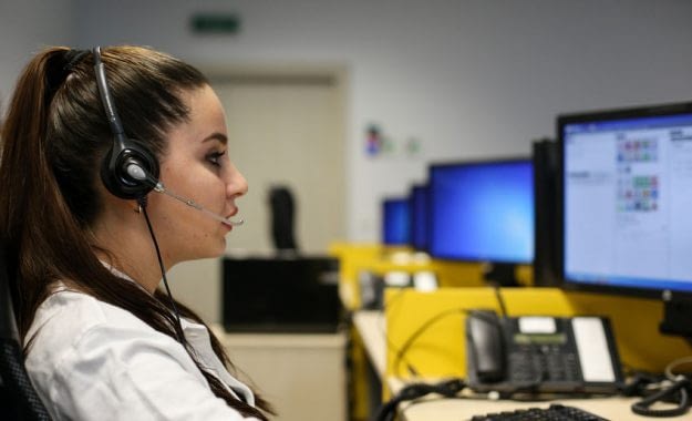 Young woman with the headset sits in front of the computer screen in a call centre and manages an assistance case